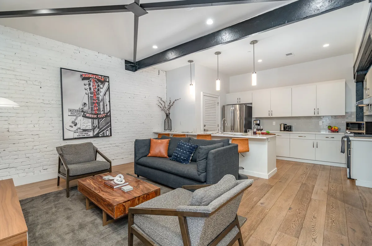 A cozy living area featuring a sofa with orange and blue cushions, a wood coffee table, and colorful artwork. The space feels intimate yet ready for group gatherings or casual relaxation, blending style and comfort.