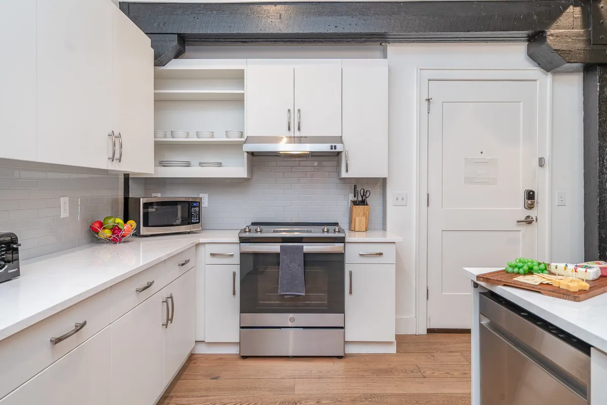 A welcoming kitchen scene with a stainless steel stove, white cabinetry, and countertops adorned with snacks ready for sharing. The layout offers both functionality and warmth, ideal for hosting and preparing communal meals.