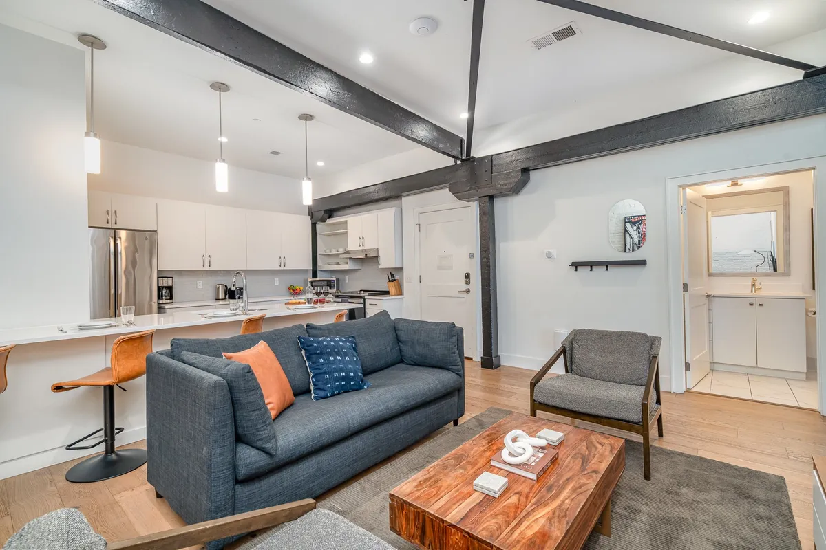An open-plan living space with a cozy sofa and coffee table adjacent to a well-equipped kitchen island with additional bar stools. The setup encourages group interaction, whether lounging or prepping food and drinks in the kitchen area.