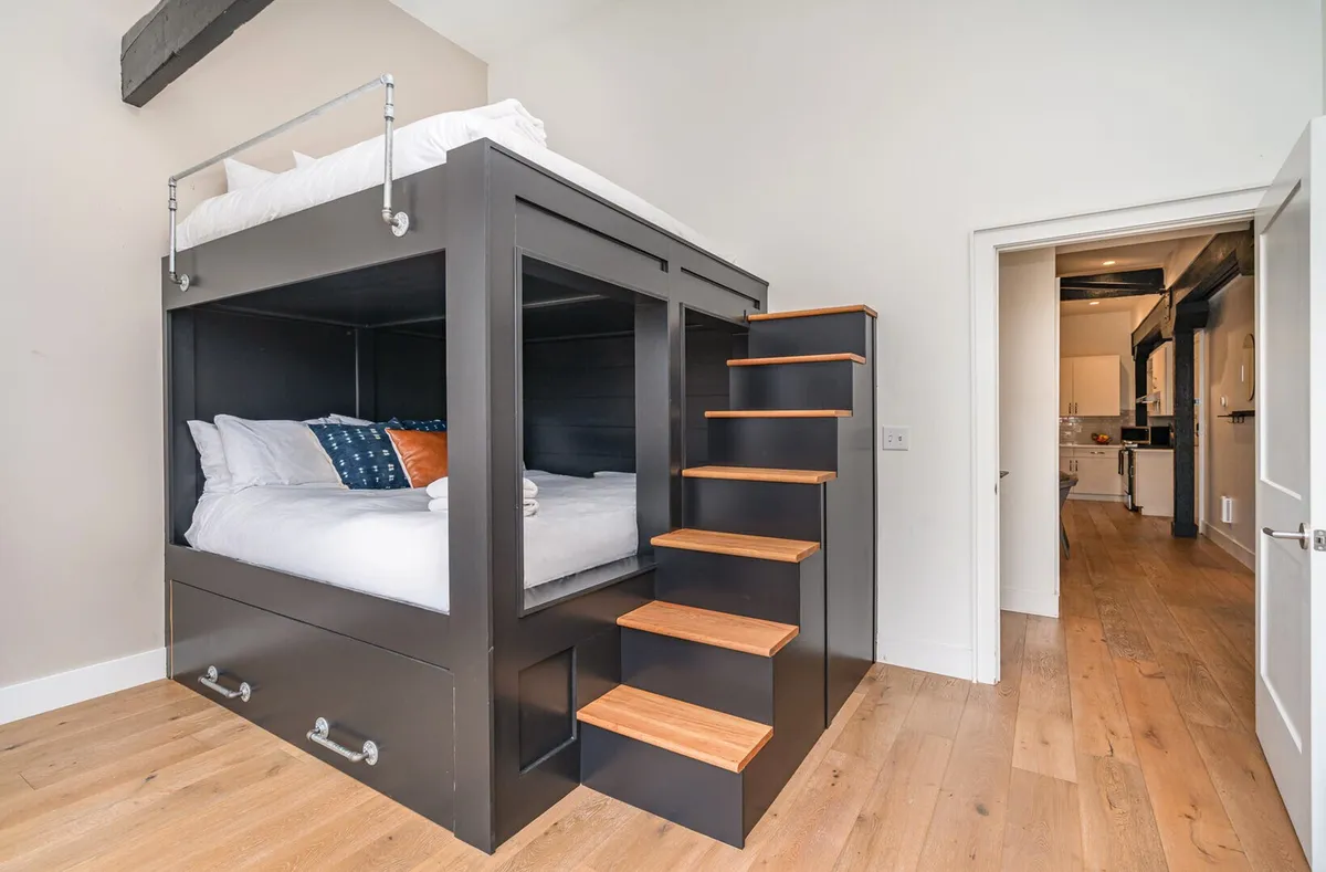 A welcoming bedroom featuring a playful bunk bed setup with a staircase and decorative pillows. The design suggests ample sleeping accommodations perfect for groups or families, and the overall vibe is cheerful and inviting.