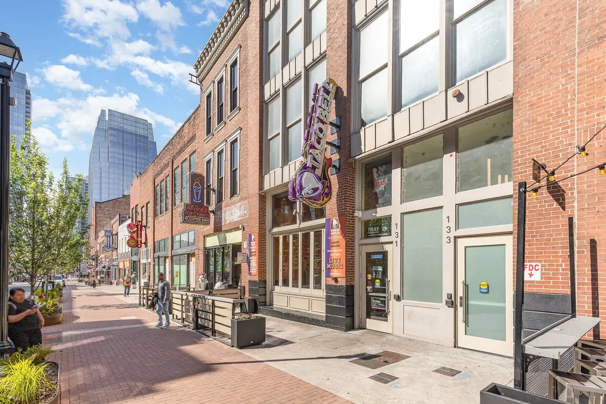 This energetic street scene features people walking past various storefronts and a prominent Taco Bell sign, capturing the lively and social atmosphere of downtown. The image suggests walkability and easy access to a range of local dining and entertainment options.