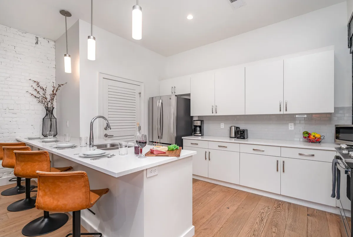 A contemporary kitchen with a central island, surrounded by bar stools, modern stainless steel appliances, and a vase of fresh flowers. The kitchen is staged for entertaining, with ample counter space perfect for group gatherings and snack preparation.